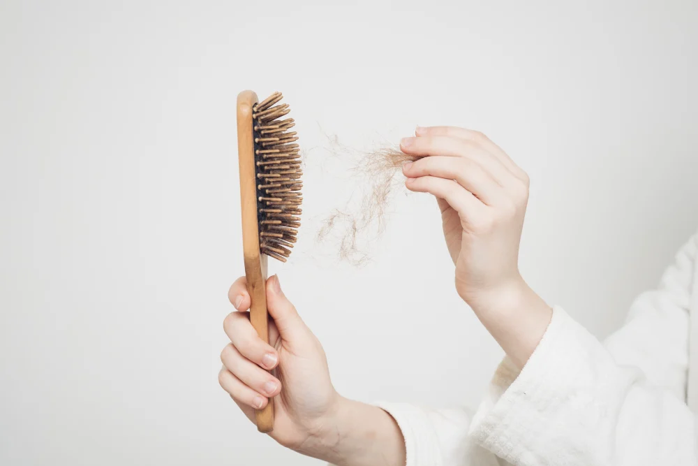 Woman noticing excessive hair strands on the comb due to hair loss. 